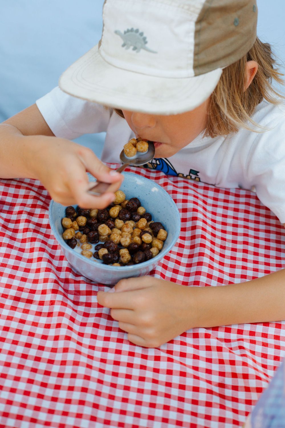 Child eating a spoonful of Cheeky Pete's at an outdoor table